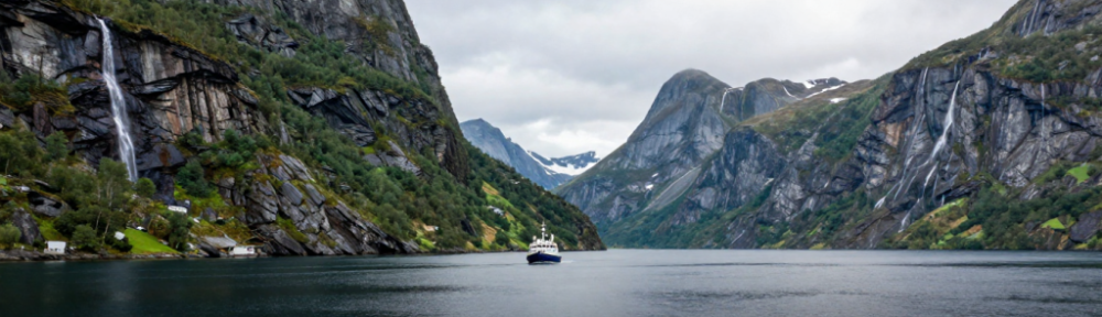 fiordos de Noruega con barco navegando entre montañas y cascada